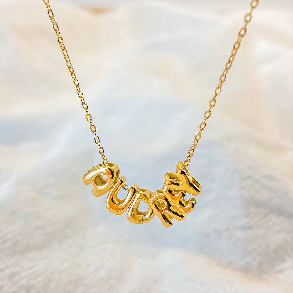 Gold necklace with 'PUDDING' pendant on a soft background