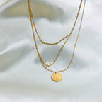 Gold stainless steel multilayer necklace with custom name pendant, bead chain, and textured disc charm displayed on a white surface.