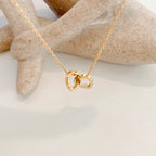 Stainless steel 18K gold PVD plated interlocking heart pendant necklace with minimalist geometric design on fine chain.