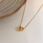 Stainless steel 18K gold PVD plated interlocking heart pendant necklace with minimalist geometric design on fine chain.
