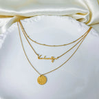 Gold stainless steel multilayer necklace with custom name pendant, bead chain, and textured disc charm displayed on a white surface.
