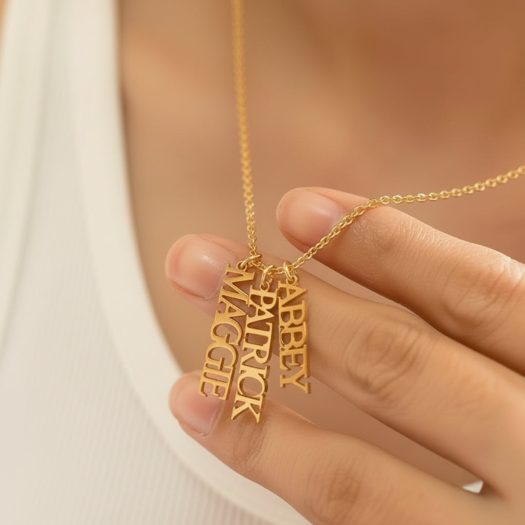 Personalized vertical name necklace in stainless steel with multiple custom name pendants, adjustable 40+5 cm chain, gold finish shown on model.
